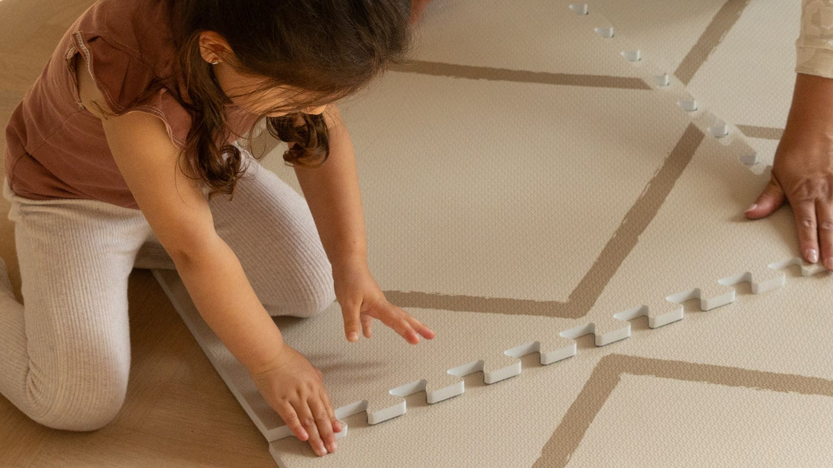 Kinder legen gemeinsam mit einem Erwachsenen die Puzzleplatten einer Eeveve Spielmatte Beni Herbstgold auf dem Holzboden zusammen